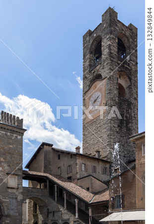 Medieval stone Civic Tower of Bergamo framed by historic rooftops and bright clear blue sky 132849844