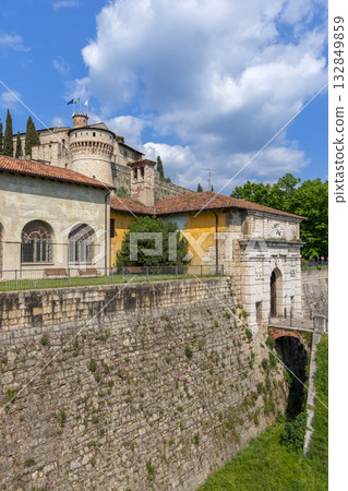 Massive stone walls and arched gateway of Brescia Castle rise below Torre dei Prigionieri tower Massive stone walls and arched gateway of Brescia Castle rise below Torre dei Prigionieri tower 132849859