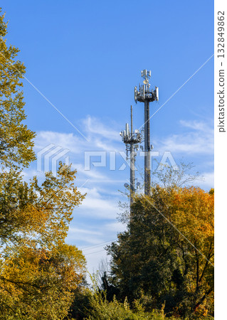 Tall metal antennas stand over autumn forest reaching vivid blue sky with drifting white clouds 132849862