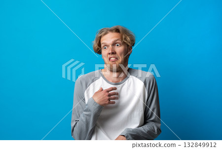 Disgusted man in gray and white shirt reacting with unpleasant facial expression on blue background Disgusted man in gray and white shirt reacting with unpleasant facial expression on blue background 132849912