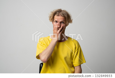 Surprised young man in yellow shirt covering mouth with hand during studio portrait session 132849933
