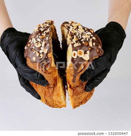 Hands in gloves holding sliced hazelnut chocolate Christmas panettone, festive dessert 132850447