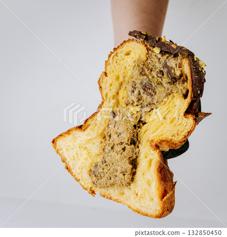 Hand holding sliced nut cream filled Christmas panettone, festive artisan dessert 132850450