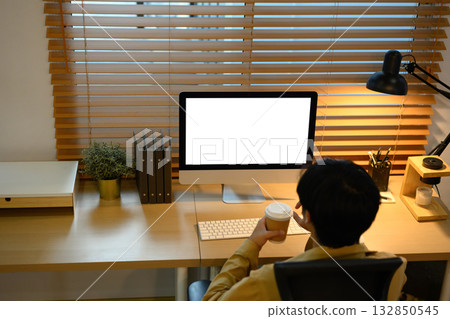 Creative man working on computer with blank screen and holding coffee cup 132850545