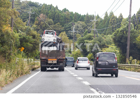 A truck driving on a two-lane road. A large truck that appears to be overloaded and carrying a large number of scrapped vehicles. 132850546