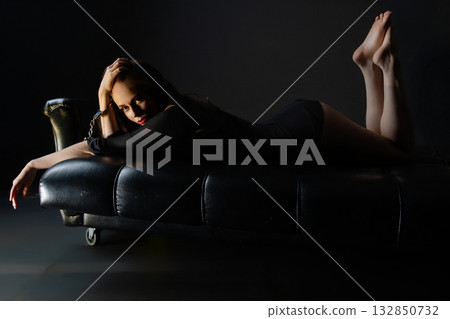 Model relaxing on a black couch in a dimly lit studio setting during a photoshoot Model relaxing on a black couch in a dimly lit studio setting during a photoshoot 132850732