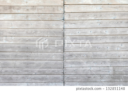 A close-up of gray, weathered wooden planks with a narrow central seam A close-up of gray, weathered wooden planks with a narrow central seam 132851148