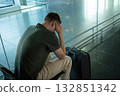 Young man with suitcase sitting in airport terminal looking upset, stressed and disappointed. Concept of flight delay, cancellation or travel problems. 132851342