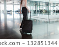 Young woman walking through airport terminal with black suitcase, motion blur. Concept of independent travel, modern lifestyle and seamless mobility. Photo in motion, soft focus. 132851344