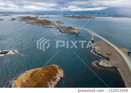 Arch of Atlantic ocean road reveals elegant span of Storseisundet bridge. Calm waters emphasize vastness and peaceful isolation of Norwegian coast Arch of Atlantic ocean road reveals elegant span of Storseisundet bridge. Calm waters emphasize vastness and peaceful isolation of Norwegian coast 132851948