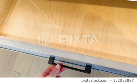 An open kitchen drawer reveals a clean, empty wooden interior. The drawer is built into modern cabinetry, and its light wood contrasts with the darker outer panel. 132851987