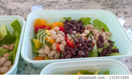 Close-up of a meal prep salad in a plastic container featuring black beans, white beans, yellow bell pepper, and greens. The image is bright and inviting. Close-up of a meal prep salad in a plastic container featuring black beans, white beans, yellow bell pepper, and greens. The image is bright and inviting. 132851989