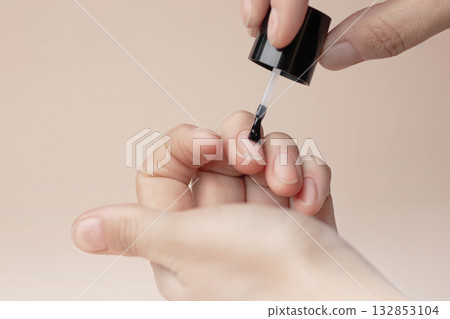 Manicure with colorless protective varnish. Woman paints her nails. Nude background copy space photo close up 132853104