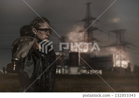 Woman against burning nuclear power plant. Young woman in a chemical protection suit 132853343