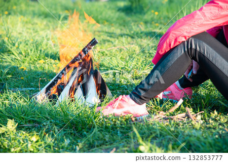 Woman sitting on the grass near a burning fire 132853777