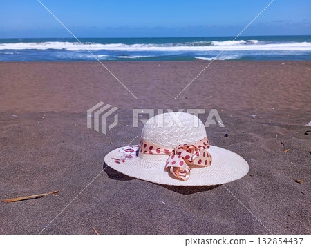 White Summer Hat Lying on Dark Sand at the Beach Shore White Summer Hat Lying on Dark Sand at the Beach Shore 132854437