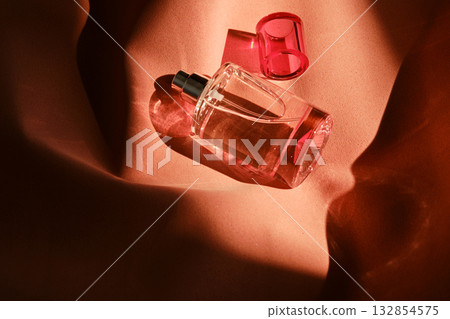 A pink perfume bottle on a soft reddish background. A pink perfume bottle on a soft reddish background. 132854575