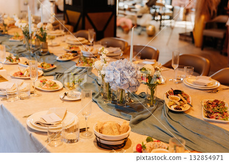 Elegant banquet table with blue hydrangea centerpieces and appetizers in warm restaurant Elegant banquet table with blue hydrangea centerpieces and appetizers in warm restaurant 132854971