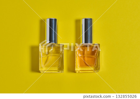 Square perfume bottle with a silver metal cap. The bottle is centered on a bright yellow background 132855026