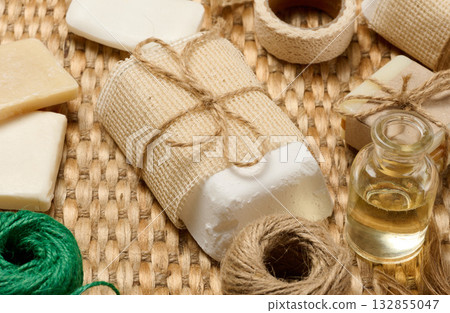 Natural handmade soap bars with various craft supplies on a woven mat. The soap bars are wrapped in burlap and twine. 132855047