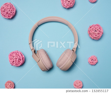 Pink wireless headphones in the center and pink decorative rattan balls on a bright, light blue background. 132855117