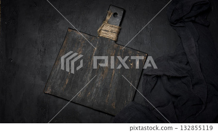 A vintage black cutting board with a handle tied with twine and dark cheesecloth on a black textured background. 132855119
