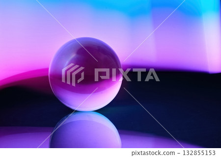 Mystical Orb. A glass sphere reflecting vibrant purple and blue hues on a smooth surface. 132855153