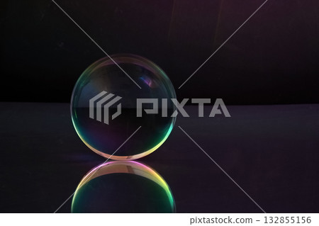 Ethereal Sphere. A glowing glass sphere with rainbow hues, reflecting on a sleek surface against a dark backdrop. Ethereal Sphere. A glowing glass sphere with rainbow hues, reflecting on a sleek surface against a dark backdrop. 132855156