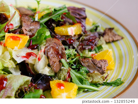 Salad with chicken liver, orange cherry sauce and arugula leaves Warm salad with fried chicken liver, cranberries and salad mix with orange dressing on a grey concrete. Healthy or diet food.  132855249
