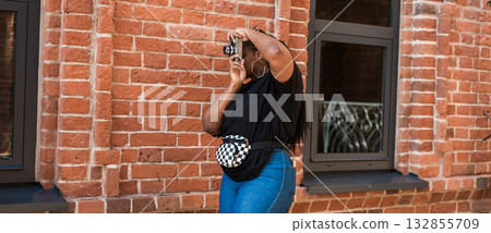 African, american woman photographing building with vintage camera outdoors. Banner with copy space. Exploration, creative process, and visual storytelling in city atmosphere. African, american woman photographing building with vintage camera outdoors. Banner with copy space. Exploration, creative process, and visual storytelling in city atmosphere. 132855709