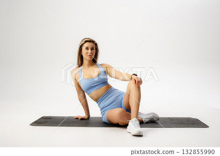 Fitness enthusiast poses on workout mat in stylish athletic gear during indoor exercise session 132855990