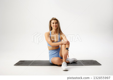 Fitness enthusiast stretches on yoga mat in minimalistic studio during daytime training session Fitness enthusiast stretches on yoga mat in minimalistic studio during daytime training session 132855997