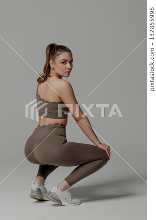 Fitness enthusiast performing a squat in stylish activewear during a studio session 132855998