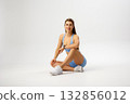 Fit woman sitting gracefully in activewear, showcasing strength and style during a fitness photoshoot in a minimalist studio setting 132856012