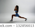 Woman performs a lunging exercise in a minimalistic studio, showcasing strength and focus during a workout session 132856013