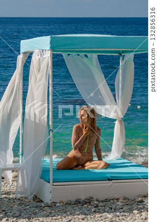 Woman beach cabana, a woman sits on a tranquil pebble beach cabana by the blue sea 132856316