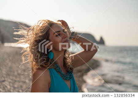 Woman, beach, sunset. Beautiful woman enjoying serene sunset on a pebble beach, wind gently blowing her curly hair, copy space. 132856334