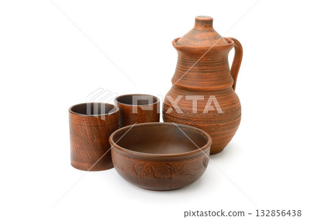 Set of traditional earthenware pottery including jug, cups, and bowl made of brown clay with carved patterns isolated on white background 132856438