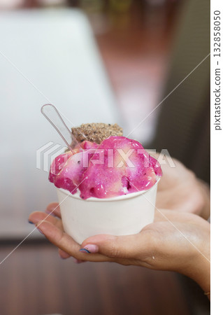 Vibrant Pink Artisan Gelato in Paper Cup Held by Hand, Close-Up Dessert with Spoon and Cookie Topping Vibrant Pink Artisan Gelato in Paper Cup Held by Hand, Close-Up Dessert with Spoon and Cookie Topping 132858050