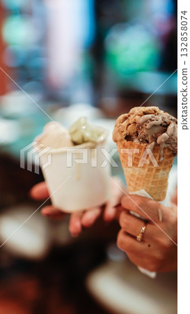 Artisan Gelato in Cone and Paper Cup Held by Hands, Close-Up Dessert with Soft Bokeh Background Artisan Gelato in Cone and Paper Cup Held by Hands, Close-Up Dessert with Soft Bokeh Background 132858074