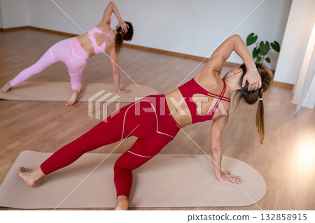 Active women execute coordinated side planks with trainer guidance in welllit studio setting Active women execute coordinated side planks with trainer guidance in welllit studio setting 132858915