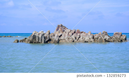 Dramatic Rocky Outcrop Formation Rises from Calm Blue Sea Water Under a Clear Sky Dramatic Rocky Outcrop Formation Rises from Calm Blue Sea Water Under a Clear Sky 132859273