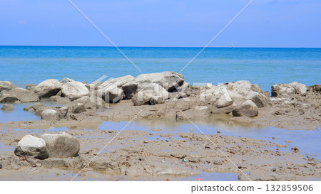 Coastal View at Low Tide Showing Mounds of Rocks and Muddy Shoreline under Blue Sky 132859506