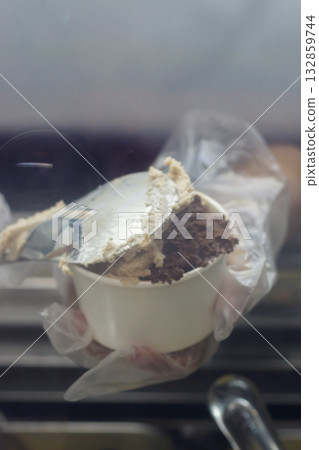 Close up of hand scooping chocolate and coffee gelato into cup at ice cream shop display counter showing creamy texture and artisan dessert preparation for cafe and lifestyle food photography 132859744