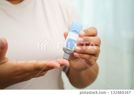 Asian woman self testing to check blood sugar level diabetes by digital lancet on finger at home. Asian woman self testing to check blood sugar level diabetes by digital lancet on finger at home. 132860167