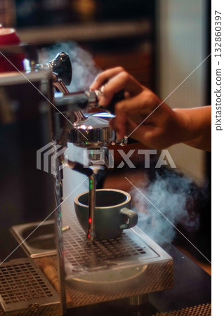 Barista preparing espresso with professional coffee machine in cafe, close up of hand making coffee with steam and hot drink cup, artisan coffee brewing process with warm lighting and cafe atmosphere Barista preparing espresso with professional coffee machine in cafe, close up of hand making coffee with steam and hot drink cup, artisan coffee brewing process with warm lighting and cafe atmosphere 132860397
