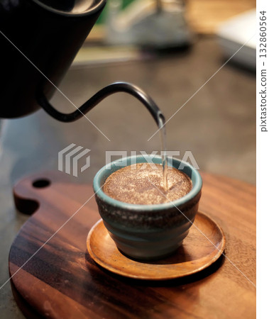 Pour-over coffee being brewed into ceramic cup with gooseneck kettle on wooden board, close-up shallow depth of field warm cozy morning coffee ritual for cafe menu and lifestyle 132860564