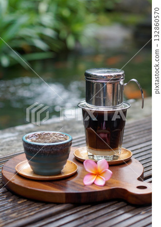Vietnamese drip coffee with condensed milk and ceramic cup on wooden board, tropical frangipani flower, outdoor cafe scene, authentic slow coffee lifestyle and warm natural atmosphere Vietnamese drip coffee with condensed milk and ceramic cup on wooden board, tropical frangipani flower, outdoor cafe scene, authentic slow coffee lifestyle and warm natural atmosphere 132860570
