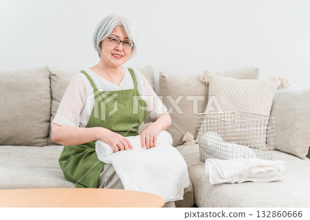 Senior Asian woman folding laundry in the living room at home (housework, housewife, full-time housewife) 132860666
