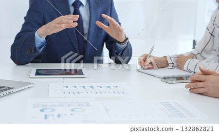 Business team collaborating in an office, analyzing financial data through digital tablets and documents during a meeting. Close up view of hands engaged in discussion and strategy planning 132862821